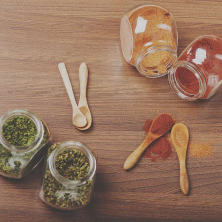 Four glass jar with spices and four wooden spoon on the table.の写真素材