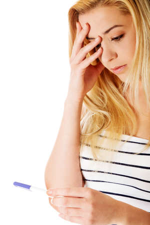 Stressed teenage girl looking on pregnancy test- isolated on white.の写真素材