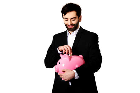 Happy handsome businessman putting a coin to piggybank.の写真素材