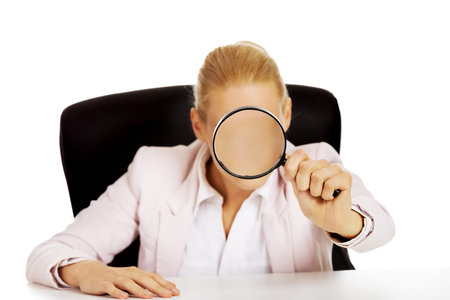 Business woman sitting behind the desk and looking into a magnifying glass.の写真素材