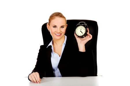 Happy business woman with alarm clock behind the desk.の写真素材