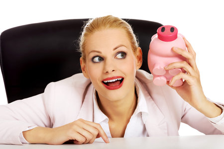 Happy business woman with a piggybank behind the desk.の写真素材