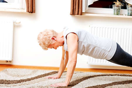 Senior woman doing yoga in living room.の写真素材