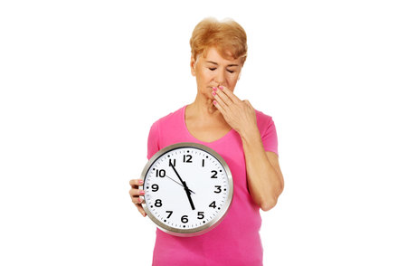 Elderly yawning woman holding big clock.