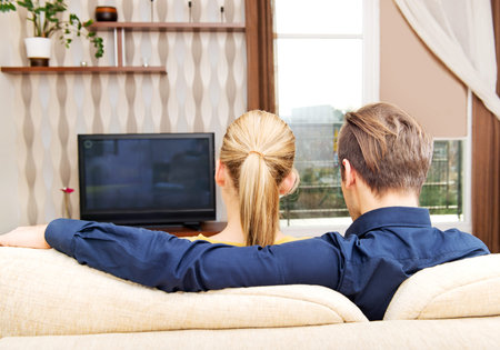 Back view of a couple watching tv at home.