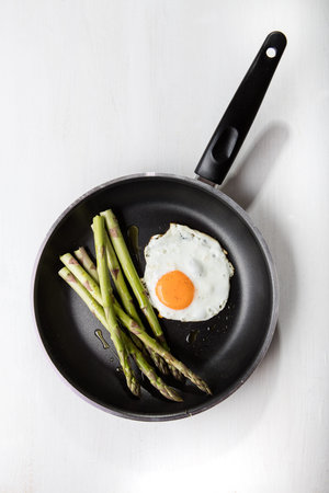 Green asparagus with fried egg on the frying pan.