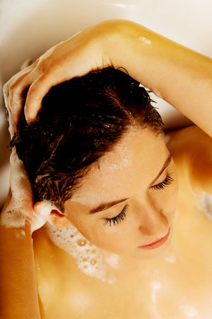 Young relaxing woman washing hair in bath.