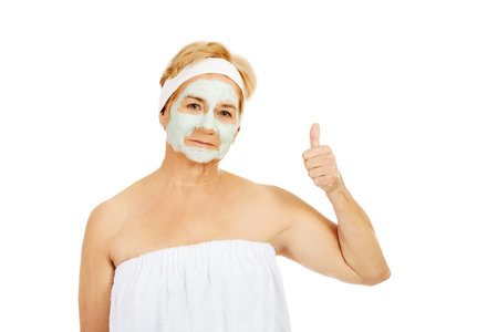 Smile elderly woman with facial mask shows thumb up.の写真素材