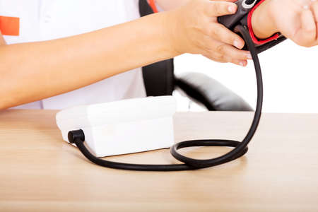 Female doctor or nurse sitting behind the desk holding blood pressure gauge.の写真素材