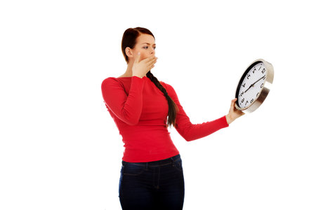 Young yawning woman holding a clock.
