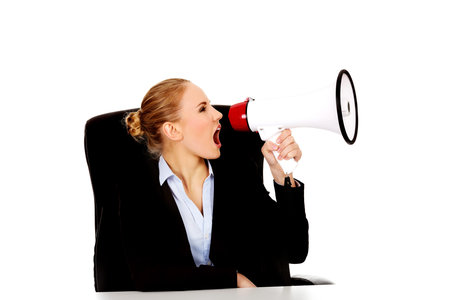 Business woman sitting behind the desk and screaming through a megaphone.の写真素材