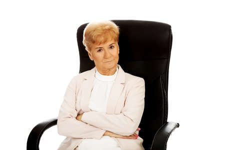 Angry elderly business woman sitting on armchair with folded arms.の写真素材