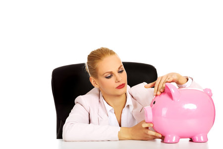 Happy business woman with a piggybank behind the desk.の写真素材