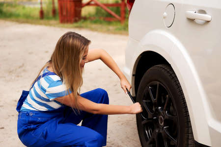 Female mechanic changing tire with wheel wrench.の写真素材