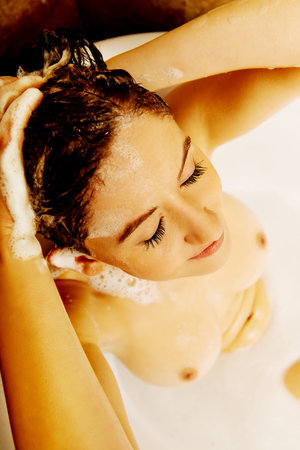 Young topless woman washing hair in bath.の写真素材