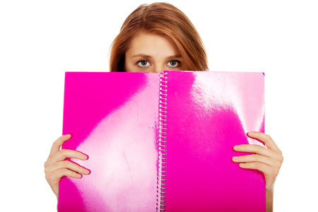 Teenage woman hiding her face behind a notebook.の写真素材