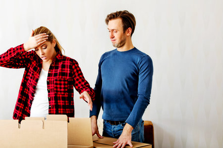Couple unpaking boxes, woman looking to inside and aghast holding her head.