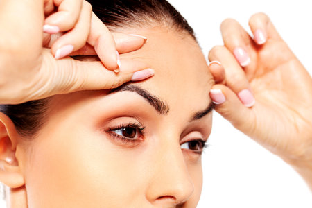 Worried young woman checking wrinkles on forehead.