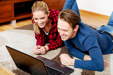 Happy couple lying on the floor with laptop.の写真素材