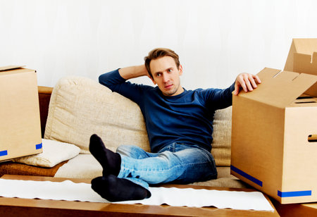 Tired man sitting on couch with cardboard boxes around.