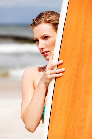 Young blond girl in bikini surfing on the beach.