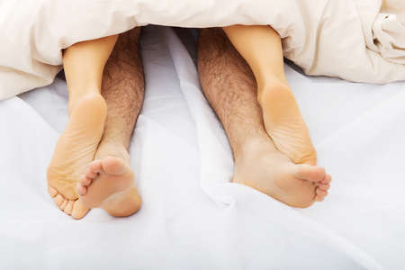 Couple's feet in bed under the quilt.の写真素材