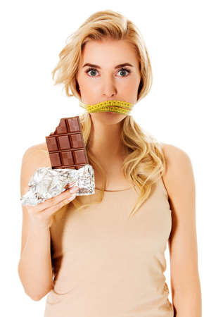 Woman with tied mouth holding bar of chocolate.の写真素材