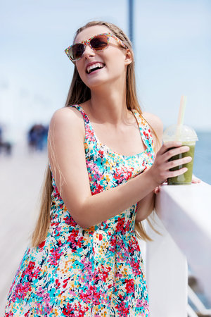 Beautiful young woman with sunglasses drinking green vegetable smoothie.
