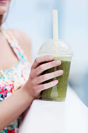 Beautiful young woman with sunglasses drinking green vegetable smoothie.の写真素材