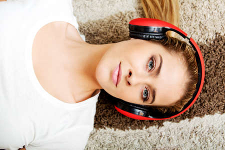 Young woman lying on the carpet and listenig a music in headphonesの写真素材