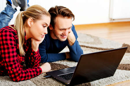Happy couple lying on the floor with laptopの写真素材