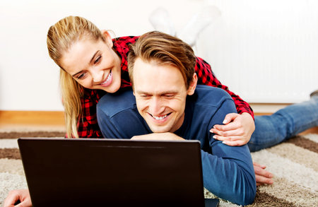 Happy couple lying on the floor with laptopの写真素材