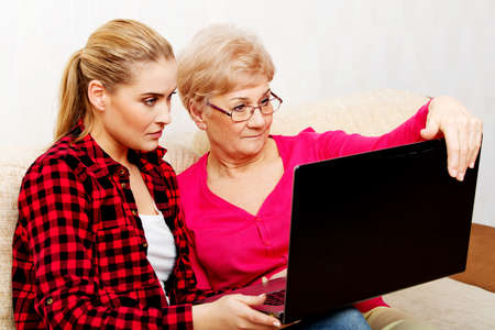 Mother and daughter sitting on couch and watching something on laptopの写真素材