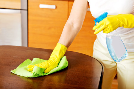 Elderly woman in yellow gloves cleaning table