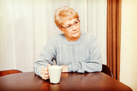 Senior woman sitting at the desk and drinking coffee or tea.の写真素材