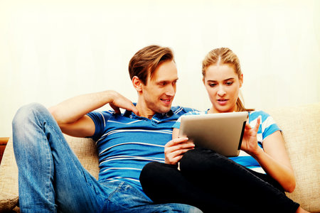 Young couple sitting at home and looking for something on tablet.の写真素材
