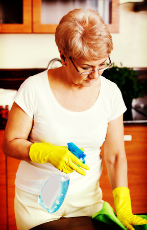 Elderly woman in yellow gloves cleaning table.の写真素材