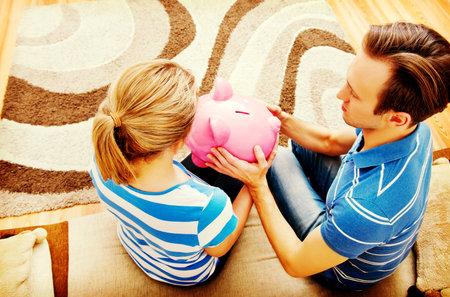 Back view of couple sitting on sofa with piggy bank.の写真素材