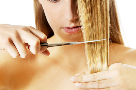 Attractive young woman is cutting her long natural hair.
