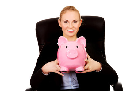 Business woman sitting on armchair and holding piggybankの写真素材