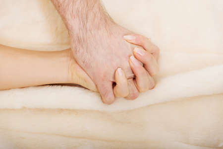 Hands of female and male lying on bedの写真素材