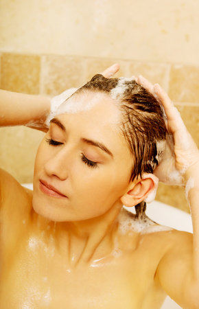 Young relaxing woman washing hair in bath