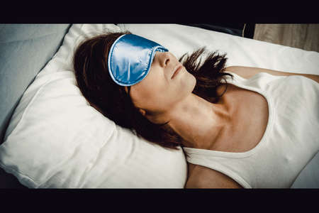 Woman sleeping in bed with eyes band.の写真素材