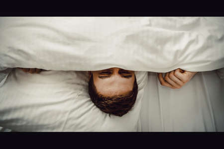 Funny man hiding in bed under the sheets.の写真素材