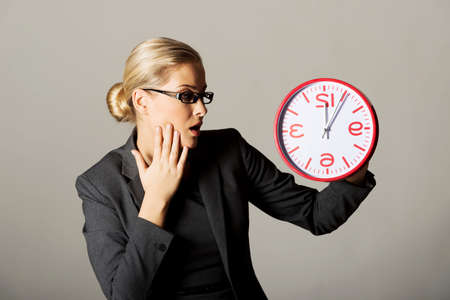 Surprised businesswoman holding a big clockの写真素材