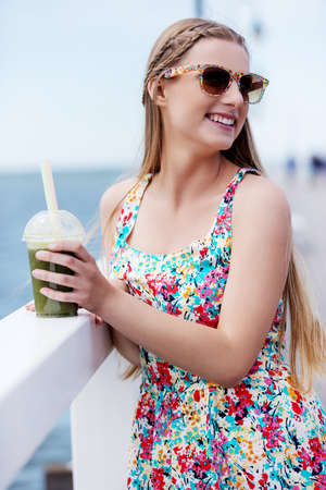 Beautiful young woman with sunglasses drinking green vegetable smoothie.の写真素材