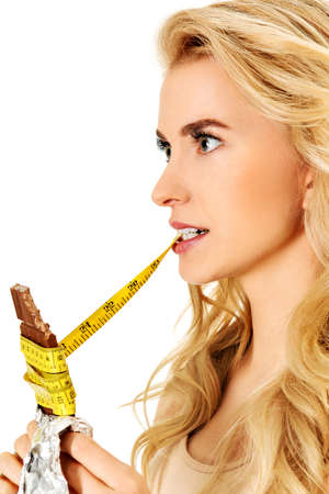 Young woman holding chocolate and eating measure tapeの写真素材