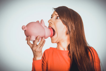 Student woman trying to eat a piggybank.の写真素材