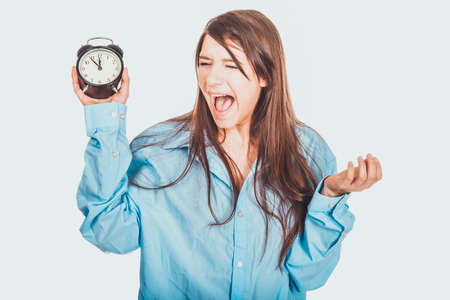 Young woman in big shirt holding alarm clock.の写真素材