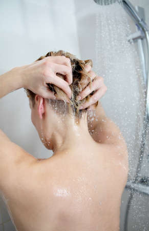 Back view of beautiful naked young woman taking showerの写真素材